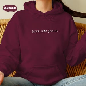 May include: Maroon hoodie with the text "love like jesus" in white. The hoodie has a drawstring hood and a front pocket. The word "MAROON" is in a maroon rectangle in the upper left corner.