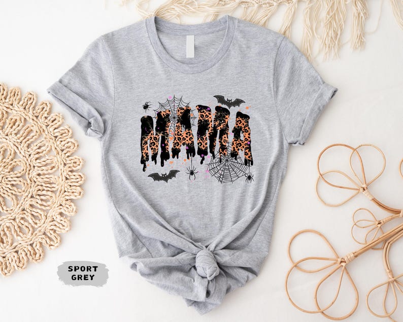 May include: Sport grey t-shirt with a Halloween-themed design. The word "MAMA" is printed in a dripping style with a leopard print pattern. The design includes bats, spiders, and spiderwebs.