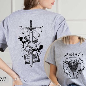May include: Sport grey t-shirt featuring a black graphic of a sword, books, and bats on the back. The front of the shirt has a circular design with the text "BASGIATH WAR COLLEGE" and a dragon illustration. A fantasy-themed apparel item.