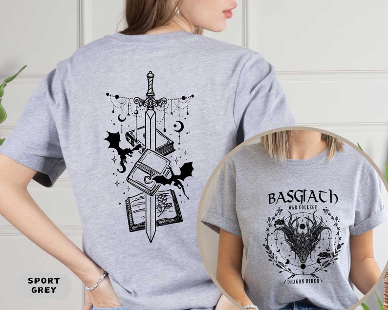 May include: Sport grey t-shirt featuring a black graphic of a sword, books, and bats on the back. The front of the shirt has a circular design with the text "BASGIATH WAR COLLEGE" and a dragon illustration. A fantasy-themed apparel item.