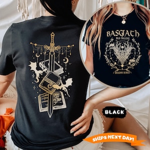 May include: Black t-shirt with a gold graphic of a sword, books, and bats. The shirt also features the text "BASGIATH WAR COLLEGE DRAGON RIDER" in a circular design. The shirt is a crew neck and short-sleeved.
