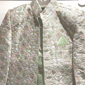 May include: A light green formal jacket and vest set with intricate floral embroidery. The jacket features a mandarin collar, button closures, and a pocket square. The embroidery includes pink, yellow, and gold accents, creating a textured, elegant look.