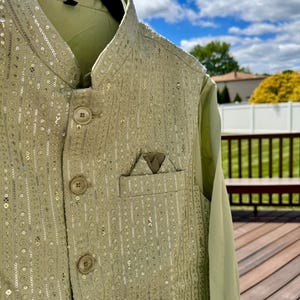 May include: A light green sleeveless vest featuring intricate vertical embroidery and silver sequin embellishments. The garment has a mandarin collar, four round buttons down the front, and a small chest pocket with a folded pocket square.