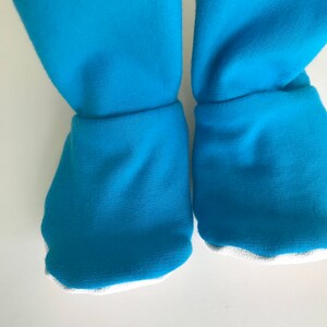 May include: A pair of blue baby booties with white trim. The booties are made of a soft, stretchy fabric.