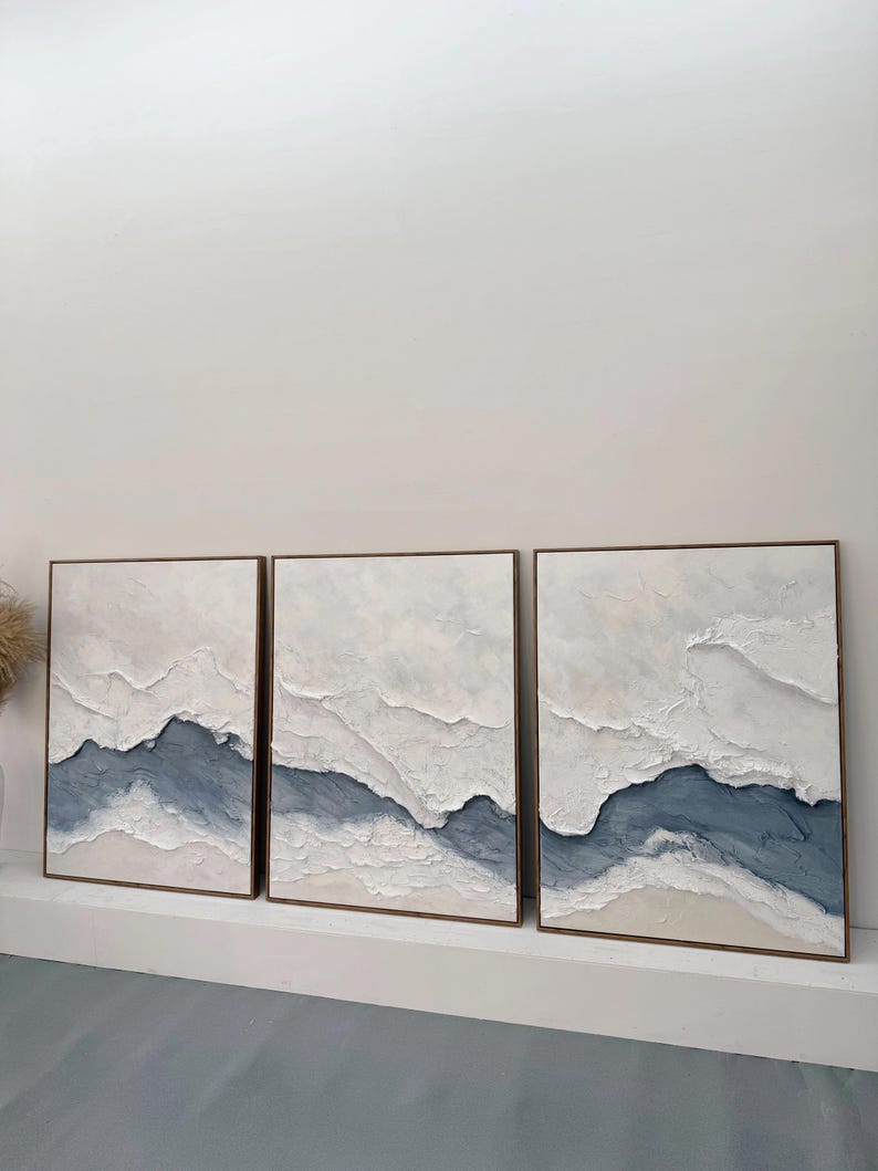 May include: A triptych of three rectangular wall art pieces featuring heavy white and blue impasto texture. Each canvas displays a layered, abstract landscape design with thick, raised white paint strokes contrasting against a deep blue base.