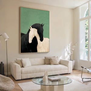 May include: A framed art print featuring two horses, one black and one white, against a green background. The horses are depicted in a minimalist style, with the black horse embracing the white horse. The artwork is displayed in a living room setting.