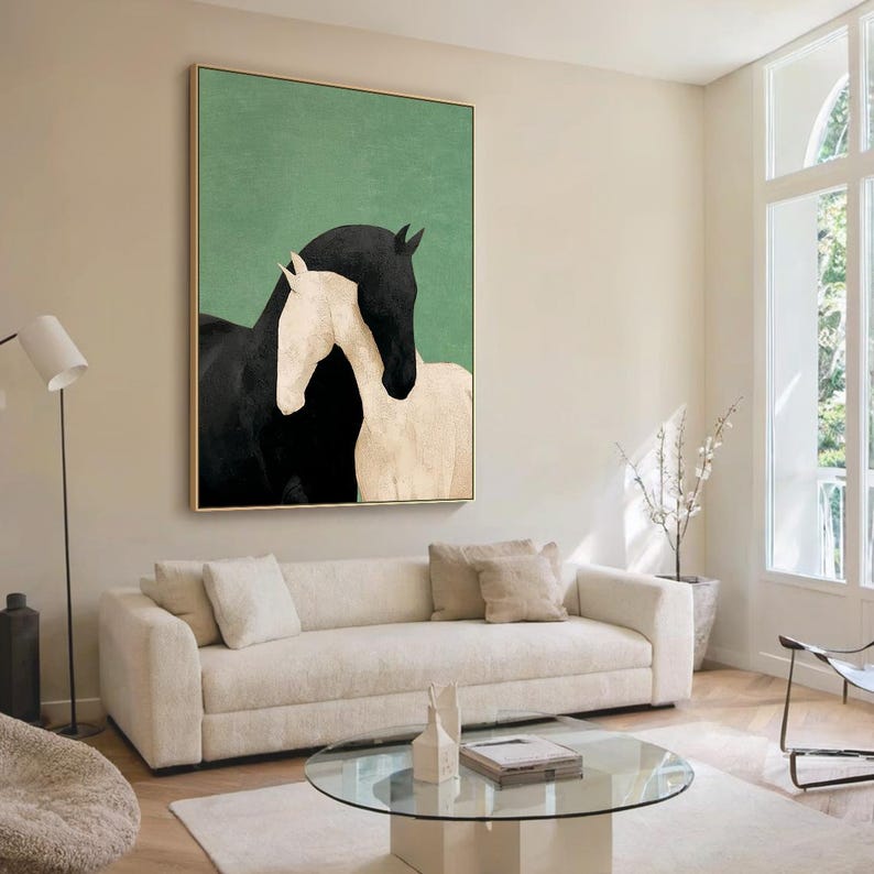 May include: A framed art print featuring two horses, one black and one white, against a green background. The horses are depicted in a minimalist style, with the black horse embracing the white horse. The artwork is displayed in a living room setting.