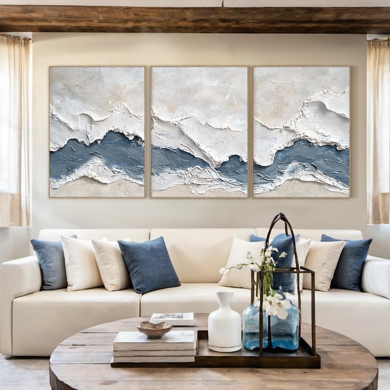 May include: A triptych wall art set featuring three rectangular canvases with heavy impasto texture. The abstract design displays layered waves of white, cream, and muted slate blue paint, creating a dimensional landscape effect across all panels.