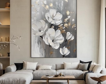 Op de afbeelding: Groot ingelijst abstract bloemenschilderij. Het kunstwerk toont witte bloemen met getextureerde bloemblaadjes tegen een grijze en gouden achtergrond. Het schilderij wordt tentoongesteld boven een grijze hoekbank in een moderne woonkamer.