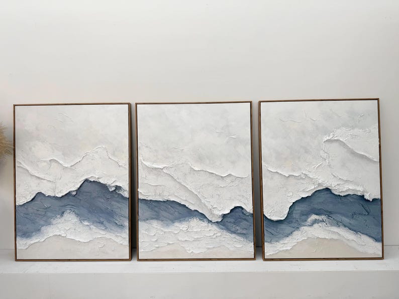 May include: A triptych of three rectangular wall art pieces featuring heavy white and blue impasto texture. Each canvas displays layered, raised white paint strokes over a deep blue base, creating a landscape effect within thin wooden frames.