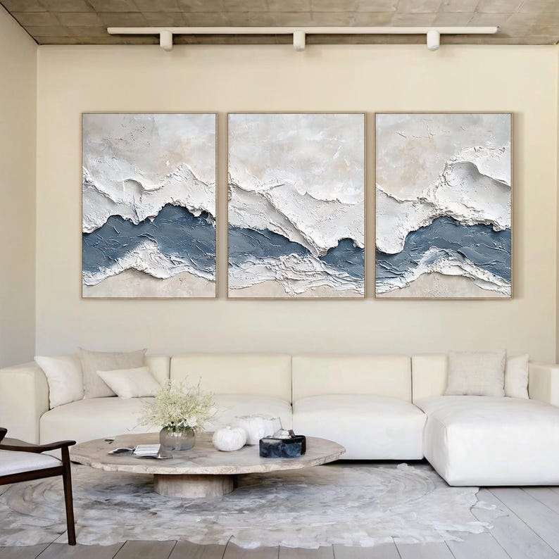 May include: A triptych of three rectangular wall art pieces featuring heavy impasto texture. Each canvas displays layered horizontal bands of white and muted blue paint, creating a raised, abstract landscape effect with visible brushstrokes.