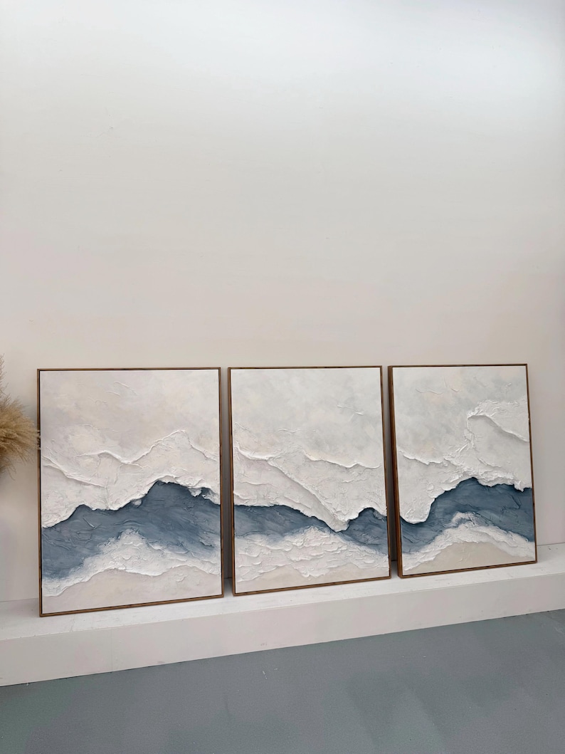 May include: A triptych of three rectangular wall art pieces featuring thick, textured white impasto paint layered over deep blue and beige tones. Each canvas is framed in a thin, light-toned wooden border, creating a cohesive landscape-inspired composition with raised, sculptural ridges across the surface.