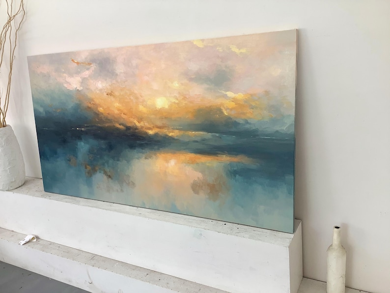 Peut inclure: Une peinture de paysage rectangulaire repr&eacute;sentant une sc&egrave;ne de coucher ou de lever de soleil avec des touches m&eacute;lang&eacute;es de jaune dor&eacute;, d'orange doux et de bleu sarcelle profond. La composition montre une ligne d'horizon au-dessus de l'eau.