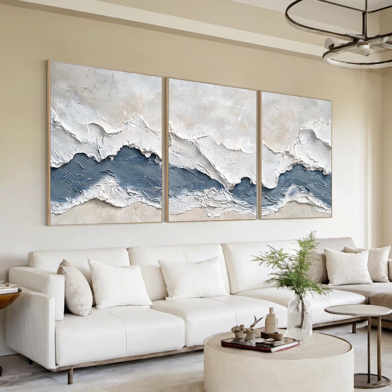 May include: A triptych wall art set featuring three rectangular canvases with heavy impasto texture. The abstract design displays layered horizontal bands of white, cream, and muted blue paint, creating a raised, rugged landscape effect.