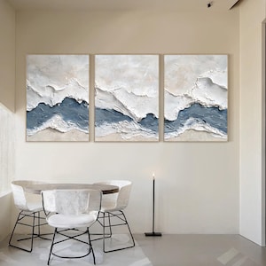 May include: A triptych of three rectangular wall art canvases featuring heavy impasto texture. The abstract composition displays layered waves of white and slate blue paint, creating a raised, three-dimensional effect across all three panels.