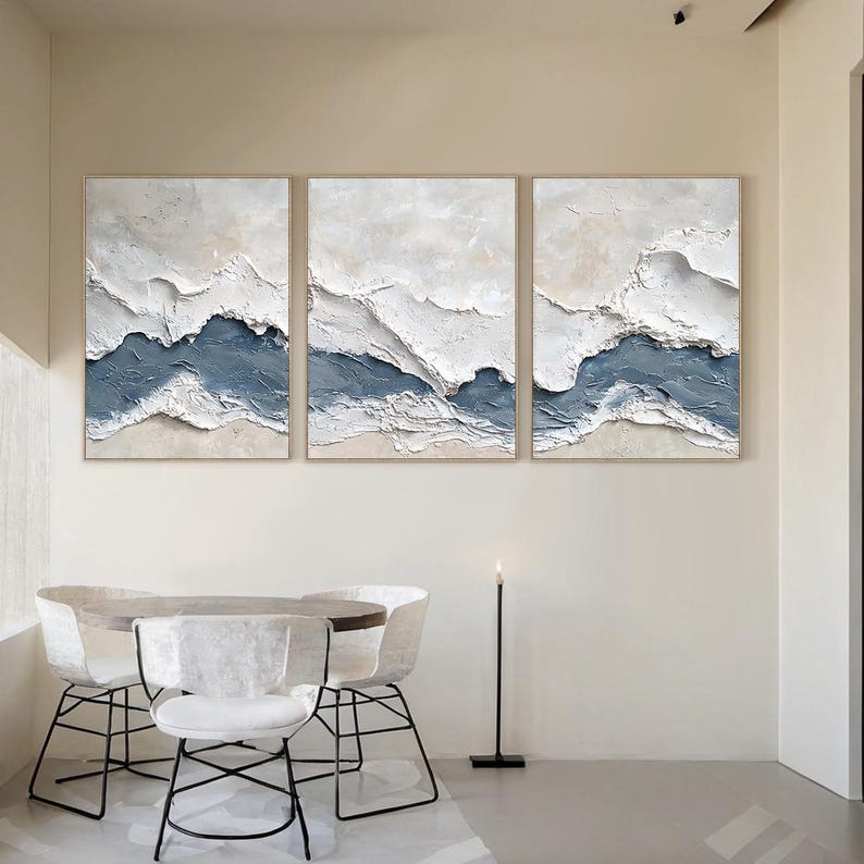 May include: A triptych of three rectangular wall art canvases featuring heavy impasto texture. The abstract composition displays layered waves of white and slate blue paint, creating a raised, three-dimensional effect across all three panels.