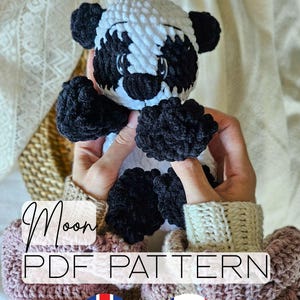 Peut inclure: Un ours panda crocheté à la main avec du fil noir et blanc. L'ours a des pattes, des oreilles et des traits du visage noirs. Le texte "Moon PDF Pattern" est affiché sur l'image, avec les drapeaux du Royaume-Uni et de la France.