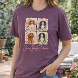 May include: A plum-colored t-shirt featuring four square images of Cavalier King Charles Spaniels surrounded by pink roses. The text "Best Dog Mom" is written in a cursive font below the images. The shirt is made of a soft material.