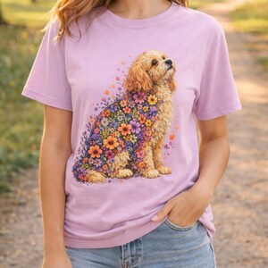 May include: A light purple t-shirt featuring a floral dog design. The dog is a golden color with a coat of colorful flowers. The shirt is a short-sleeved crew neck style.