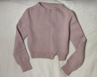 May include: A pale pink knitted jumper with long sleeves and a slightly cropped length. The jumper has a simple round neckline and a ribbed texture.