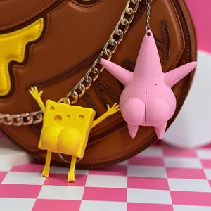 May include: A brown handbag with a yellow and brown design, featuring a silver chain strap. Two cartoon character keychains hang from the chain: a yellow SpongeBob SquarePants and a pink Patrick Star.