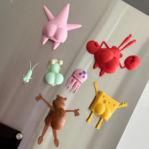 May include: A collection of colorful cartoon character magnets, including a pink starfish, a red crab, a yellow sponge, a brown bear, a green worm, a light green sea creature, and a pink jellyfish. These magnets are designed for decorative purposes.