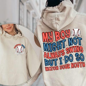 Pode incluir: Moletom com capuz cor de areia com um gráfico de beisebol na frente e atrás. A parte de trás apresenta o texto "MY BOY MIGHT NOT ALWAYS SWING BUT I DO SO WATCH YOUR MOUTH" em vermelho e azul. A frente tem um gráfico de beisebol com as palavras "Baseball Mom".