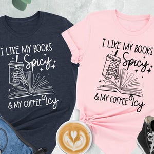 Pode incluir: Duas camisetas com um design gráfico de uma mão esquelética segurando uma xícara de café e um livro. O texto nas camisetas diz "Eu gosto dos meus livros picantes e do meu café gelado".