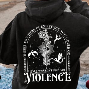 May include: Black hoodie with a white graphic on the back. The graphic features a sword, flowers, and dragons, with the text "THERE'S NOWHERE IN EXISTENCE YOU COULD GO THAT I WOULDN'T FIND YOU VIOLENCE".