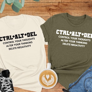 May include: Two t-shirts with the text "CTRL+ALT+DEL" and the phrase "Control your thoughts, alter your thinking, delete negativity". The shirts are in natural heather olive and white.