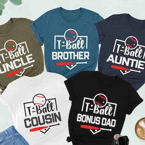 May include: Five short-sleeved t-shirts in various colors, each featuring a baseball-themed design. The shirts display the phrases "Uncle", "Brother", "Auntie", "Cousin", and "Bonus Dad" with a baseball graphic. A pair of jeans, a cup of coffee, and a pair of sneakers are also in the image.