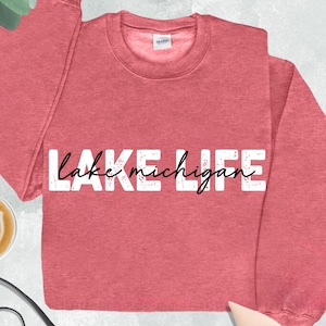Peut inclure: Un sweat-shirt &agrave; col rond rouge &eacute;carlate chin&eacute; avec le texte LAKE en lettres capitales blanches et le texte michigan en &eacute;criture cursive noire au centre. Le v&ecirc;tement poss&egrave;de des manches longues et un col c&ocirc;tel&eacute; avec une &eacute;tiquette visible.