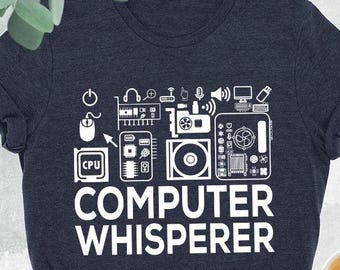 May include: Heather navy t-shirt with the text "COMPUTER WHISPERER" in white. The design includes computer-related icons. The shirt is paired with blue jeans, a black purse, and black high-top sneakers.