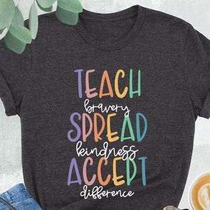May include: Dark heather grey t-shirt with the text "TEACH bravery SPREAD kindness ACCEPT difference" in rainbow colors.