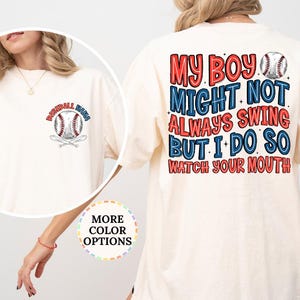 May include: Ivory-colored t-shirt with baseball-themed graphics. The front features a baseball and crossed bats with the text "Baseball Mom". The back displays the text "My boy might not always swing but I do so watch your mouth" in red and blue.