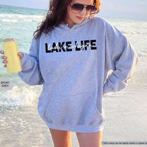 Peut inclure: Un sweat-shirt &agrave; capuche gris sport avec le texte noir LAKE LIFE et le texte cursif blanc lake michigan imprim&eacute; sur le devant. Le v&ecirc;tement comprend une poche kangourou frontale, des manches longues et une capuche avec cordons assortis.