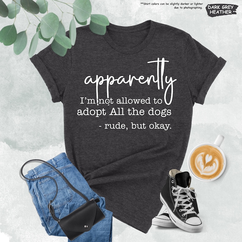 May include: Dark grey heather t-shirt with the text "apparently I'm not allowed to adopt All the dogs - rude, but okay." The image also shows blue jeans, a black purse, and black high-top sneakers.