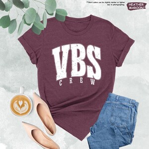 a women's vbs crew t - shirt next to a cup of coffee