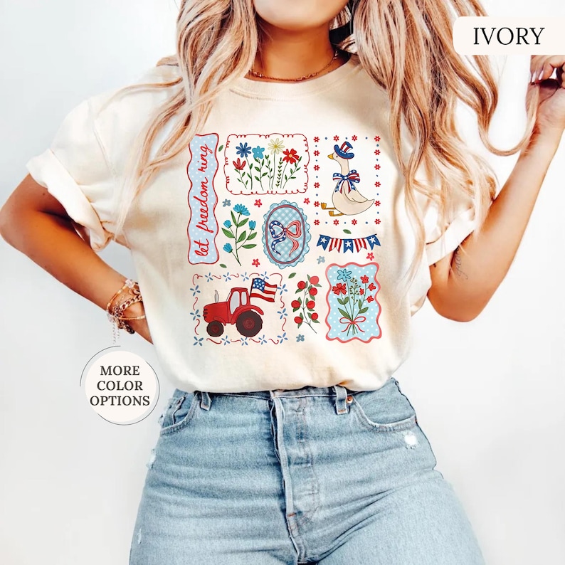 May include: Ivory-colored t-shirt with a patriotic design. The design includes a red tractor, flowers, a goose wearing a hat, and the text "let freedom ring." The shirt has short sleeves and a crew neck.