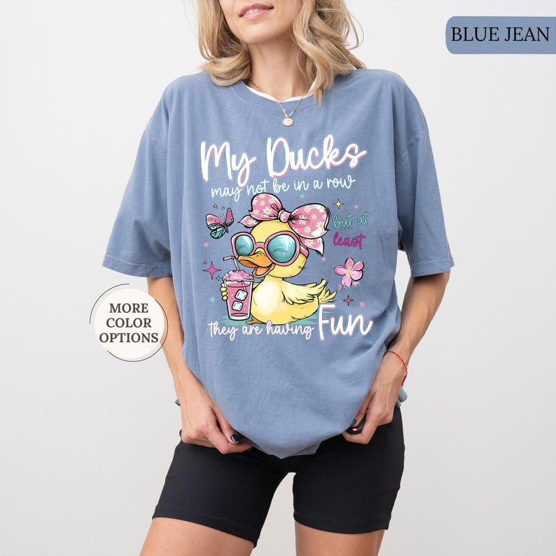 May include: Blue jean colored t-shirt with the text "My Ducks may not be in a row but at least they are having Fun." The shirt features a cartoon duck wearing sunglasses and a bow, holding a drink.