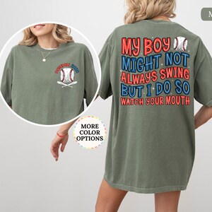 May include: Moss green t-shirt with a baseball graphic on the front and back. The front graphic says "Baseball Mom" with a baseball and crossed bats. The back says "My Boy Might Not Always Swing But I Do So Watch Your Mouth."