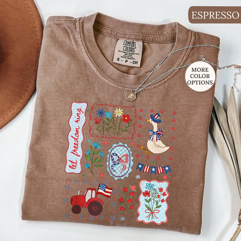 May include: Espresso-colored Comfort Colors t-shirt with patriotic-themed embroidered patches. Patches include a goose in a hat, flowers, a tractor, and the text "let freedom ring". A silver necklace is draped across the shirt.