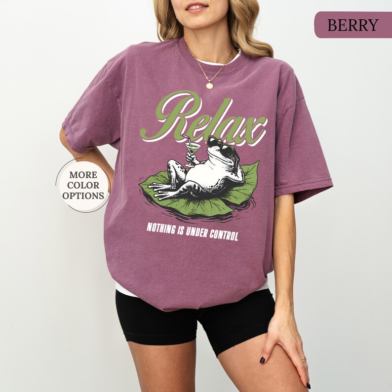 May include: Berry-colored t-shirt with a graphic of a frog relaxing on a lily pad, holding a cocktail. The word "Relax" is arched above the frog, with the phrase "Nothing is Under Control" below.