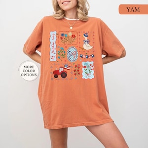 May include: Orange t-shirt with a colorful patriotic design. The design includes a tractor, flowers, a goose, and the text "let freedom ring". The shirt has short sleeves and a relaxed fit.