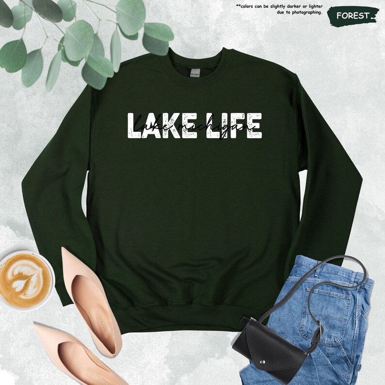 Peut inclure: Un sweat-shirt &agrave; col rond vert for&ecirc;t arborant le texte blanc vieilli LAKE LIFE avec le texte cursif Lake Michigan superpos&eacute;. Le v&ecirc;tement pr&eacute;sente des manches longues et un col c&ocirc;tel&eacute;, pr&eacute;sent&eacute; comme un article vestimentaire &agrave; plat.