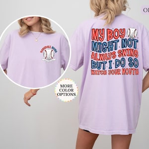 May include: Orchid-colored t-shirt with baseball-themed graphics. The front features a baseball and the words "Baseball Mom." The back displays the text "My boy might not always swing but I do so watch your mouth" in red and blue.