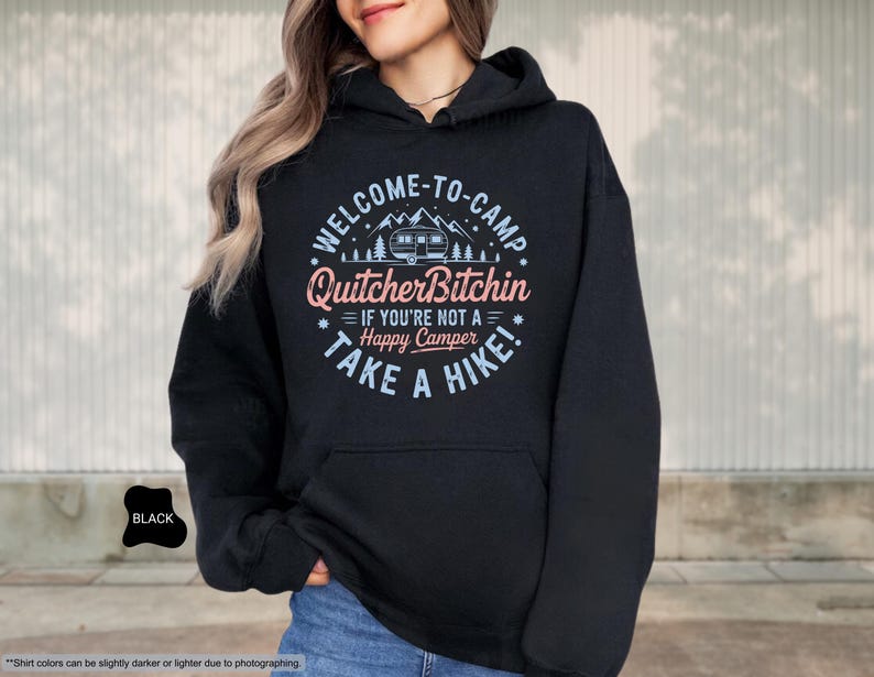 May include: Black hooded sweatshirt with the text "WELCOME-TO-CAMP Quitcher Bitchin IF YOU'RE NOT A Happy Camper TAKE A HIKE!" in a circular design. The design includes a camper, trees, and stars. The sweatshirt has a front pocket and a drawstring hood.
