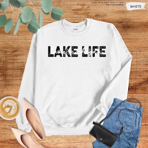 Peut inclure: Un sweat-shirt blanc &agrave; col rond avec le texte noir vieilli LAKE LIFE et le mot Michigan &eacute;crit en &eacute;criture cursive blanche au centre. Le v&ecirc;tement pr&eacute;sente des manches longues ainsi qu'un col, des poignets et un ourlet c&ocirc;tel&eacute;s.