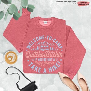 May include: Heather scarlet red sweatshirt with the text "WELCOME-TO-CAMP Quitcher Bitchin IF YOU'RE NOT A Happy Camper TAKE A HIKE!". The design includes a camper, mountains, and trees. A cup of coffee, a purse, and shoes are also in the image.