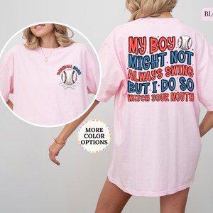 May include: A light pink t-shirt with baseball-themed graphics. The front features a baseball and crossed bats with the text "Baseball Mom". The back displays the text "My Boy Might Not Always Swing But I Do So Watch Your Mouth" with baseball graphics.